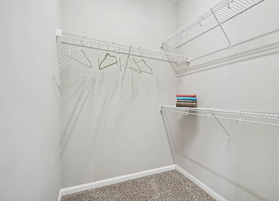 A white closet with a shelf and clothes hanging on a rod.