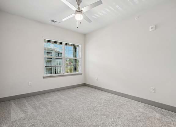A room with a ceiling fan and a window overlooking a building.