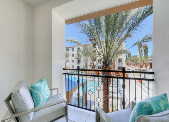 Living room with a balcony overlooking a pool and palm trees at Sola at Pacific Highlands Ranch Apartments, California