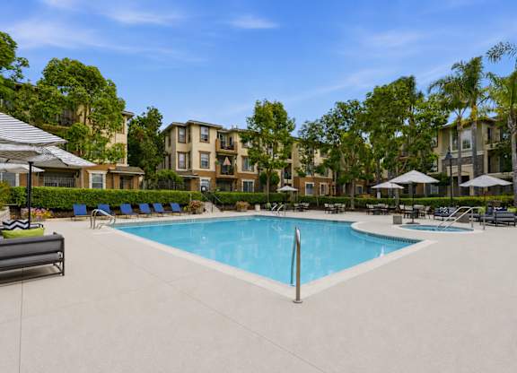 A swimming pool surrounded by lounge chairs and umbrellas in a residential area.
