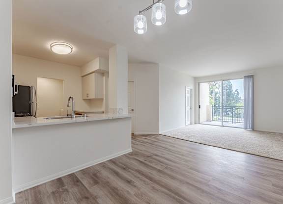 A spacious, empty room with a kitchen area and a door leading to a balcony.