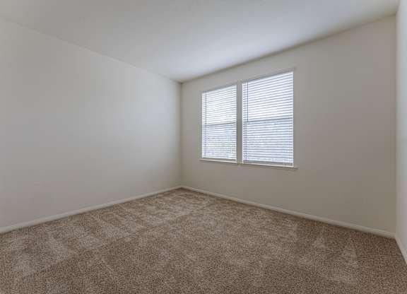 A room with a carpeted floor and a window with blinds.