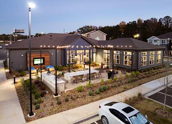 A white car is parked in front of a building with lights on.