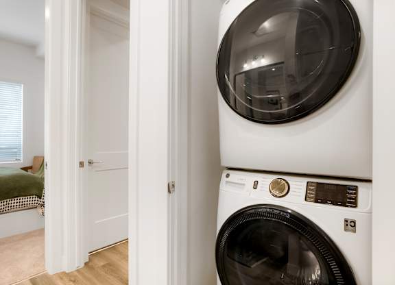 A white washing machine in a room with a bed in the background.