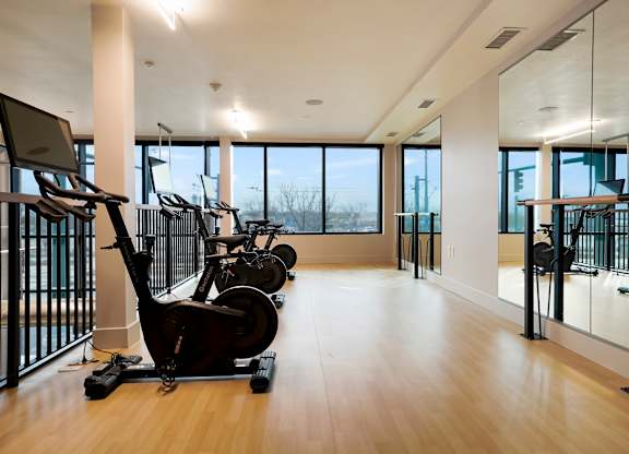 A gym with a row of exercise bikes and a row of mirrors on the wall.
