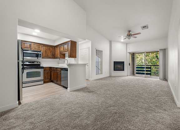 A spacious living room with a ceiling fan and a sliding glass door leading to a balcony.