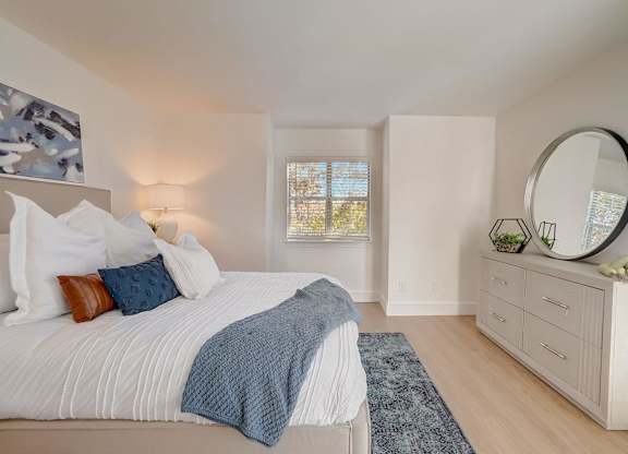 A bedroom with a large bed, a round mirror, and a window with a view of trees.