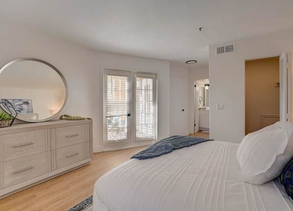 A bedroom with a large bed, a dresser with a mirror, and a window with blinds.