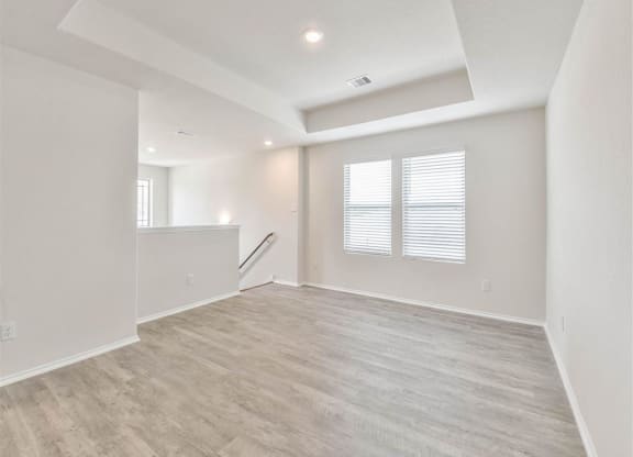 the spacious living room and dining room with white walls and wood flooring at The Village at Caney Mills, Conroe
