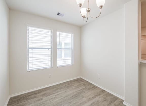 an empty room with two windows and a chandelier at The Village at Caney Mills, Conroe, TX