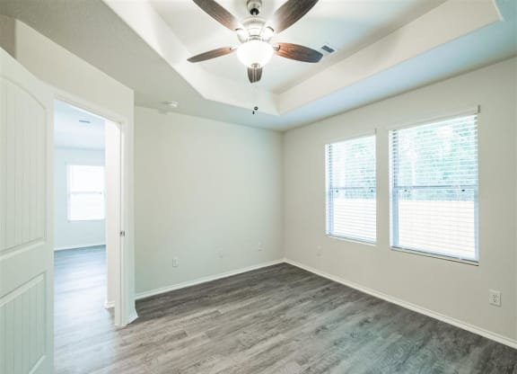 an empty living room with a ceiling fan and two windows at The Village at Caney Mills, Conroe, Texas