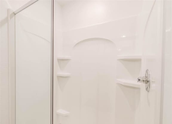 a white bathroom with a shower and shelves in it at The Village at Caney Mills, Conroe