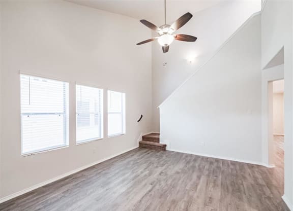an empty living room with a ceiling fan and windows at The Village at Caney Mills, Conroe, TX