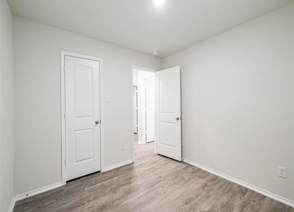 an empty living room with white walls and wood floors at The Village at Caney Mills, Conroe, TX