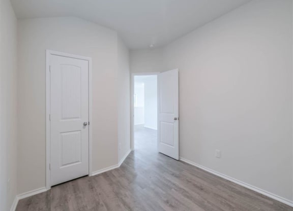 a bedroom with white walls and doors and a wood floor at The Village at Caney Mills, Conroe, TX
