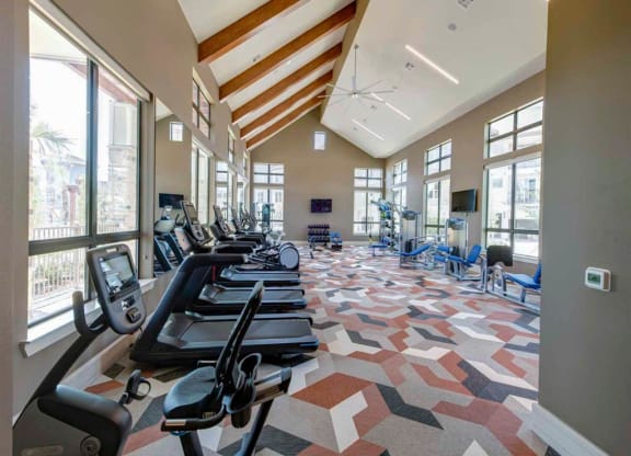 a gym with cardio equipment and large windows