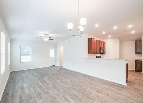 an empty living room with a kitchen and a ceiling fan