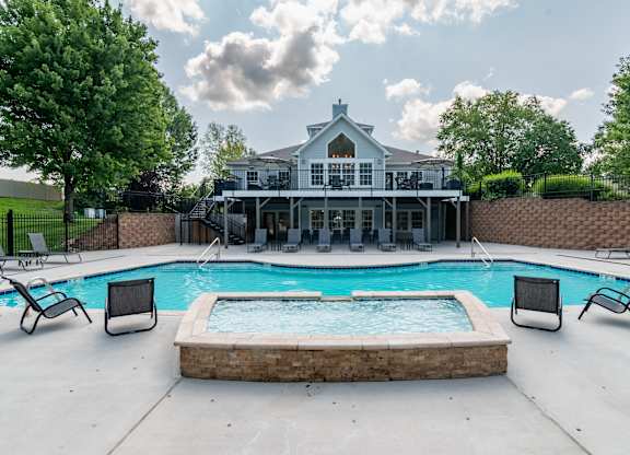 A pool with a hot tub and a house in the background.