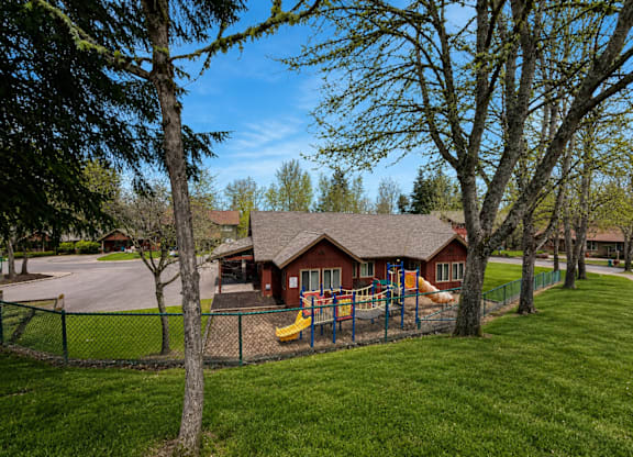 A playground with a yellow slide is in front of a red building.