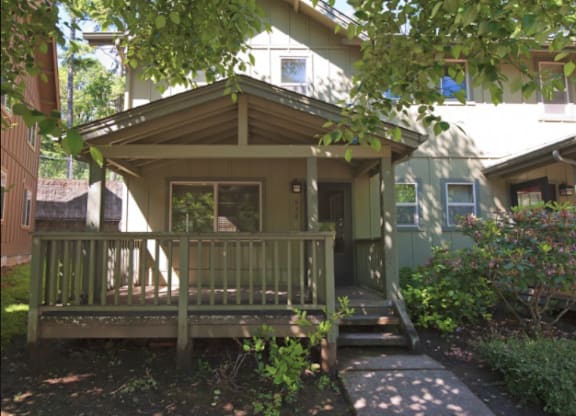 A small house with a porch and a tree in front.