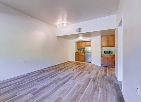 A room with wooden flooring and a kitchen area in the background.