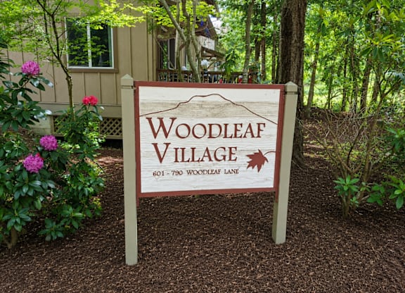 A sign that says Woodleaf Village stands in front of a house.