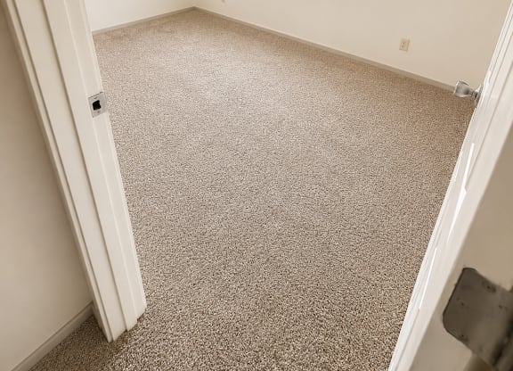 A room with a carpeted floor and a window with blinds.