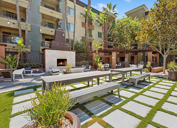A patio with a table and chairs is surrounded by a grassy area and apartment buildings at The Kitt at Warner Center Apartments, California, 91303