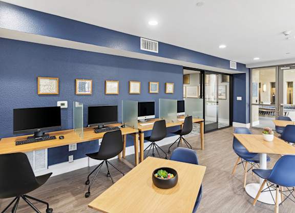A room with blue walls and wooden tables with chairs at The Kitt at Warner Center Apartments, Woodland Hills, CA