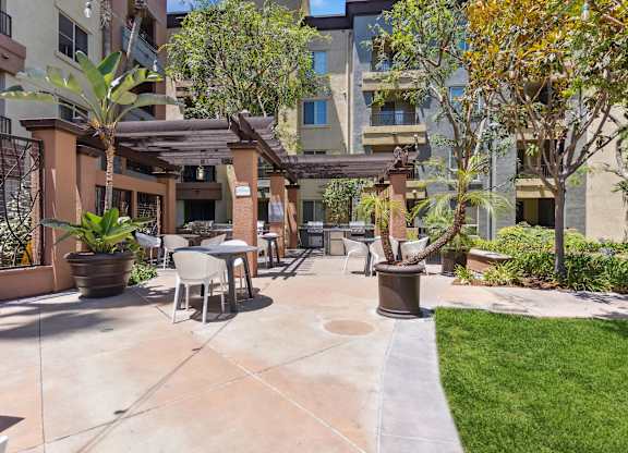 A patio area with a table and chairs surrounded by plants and trees at The Kitt at Warner Center Apartments, Woodland Hills, CA