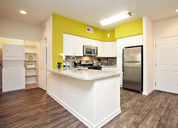 A kitchen with white appliances and a yellow accent wall at The Kitt at Warner Center Apartments, Woodland Hills 91303