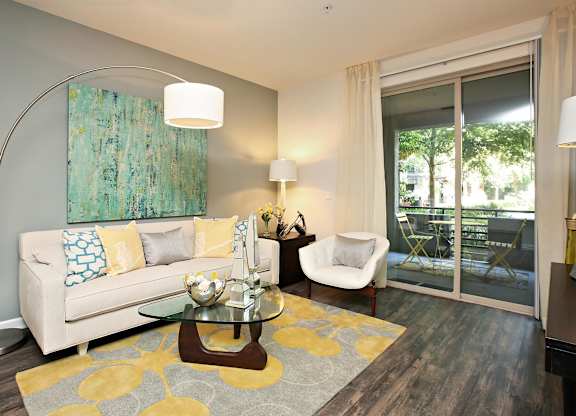 A living room with a white couch, a glass coffee table, and a painting on the wall at The Kitt at Warner Center Apartments, Woodland Hills, California