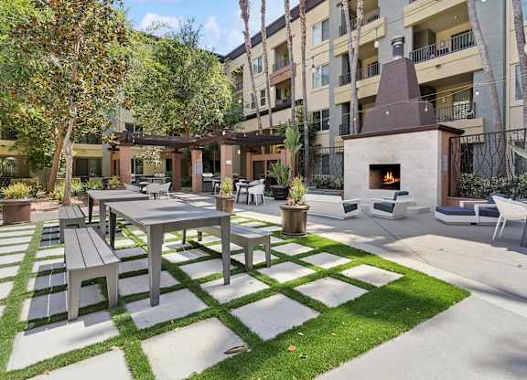 A patio with a table and chairs is surrounded by a grassy area and apartment buildings at The Kitt at Warner Center Apartments, Woodland Hills