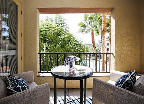 A balcony with a table and two chairs overlooking a lush green area at The Kitt at Warner Center Apartments, California