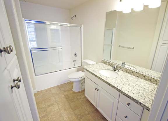 A bathroom with a toilet, sink, and mirror at The Kitt at Warner Center Apartments, California, 91303
