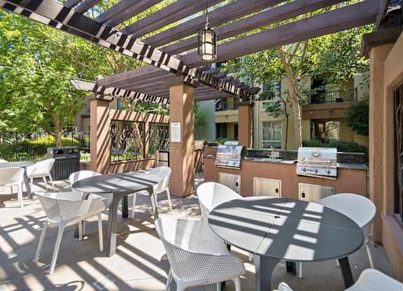A patio with white chairs and tables is covered by a striped awning at The Kitt at Warner Center Apartments, Woodland Hills, CA, 91303