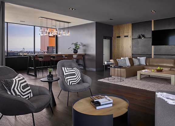 A modern living room with a grey couch, a wooden coffee table, and a large window overlooking the city.