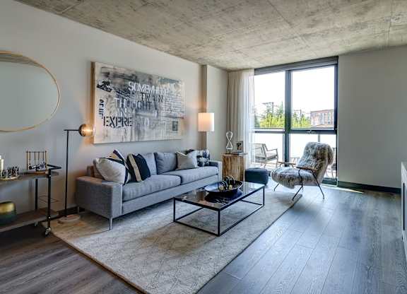A modern living room with a grey sofa, a coffee table, and a large abstract painting on the wall. at The Mason Apartments, Chicago, IL
