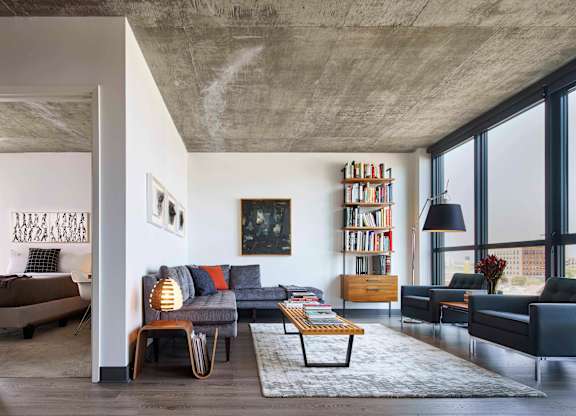 A modern living room with a concrete ceiling and a large window. at The Mason Apartments, Chicago, IL