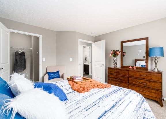 A bedroom with a bed, dresser, mirror, and lamp at Estates at Brentwood Lake Apartments, Reynoldsburg, OH