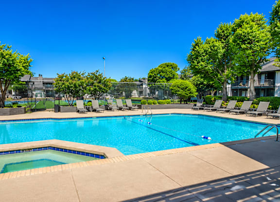 A large swimming pool surrounded by trees and lounge chairs.