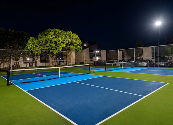 A tennis court at night with lights on.