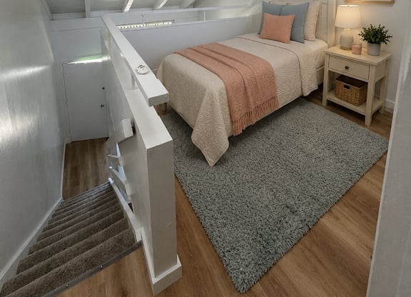 A bedroom with a bed, nightstand, and staircase.