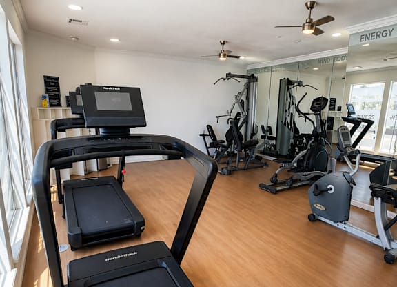 A treadmill is in the foreground of a well equipped gym.