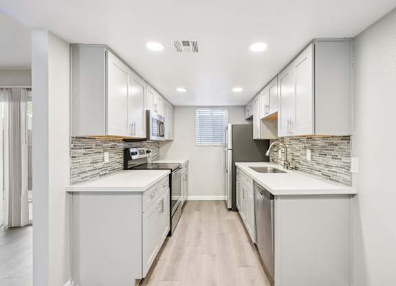 A modern kitchen with white cabinets and a wooden floor.
