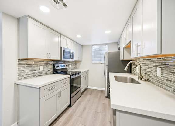 A modern kitchen with white cabinets and a stone backsplash.
