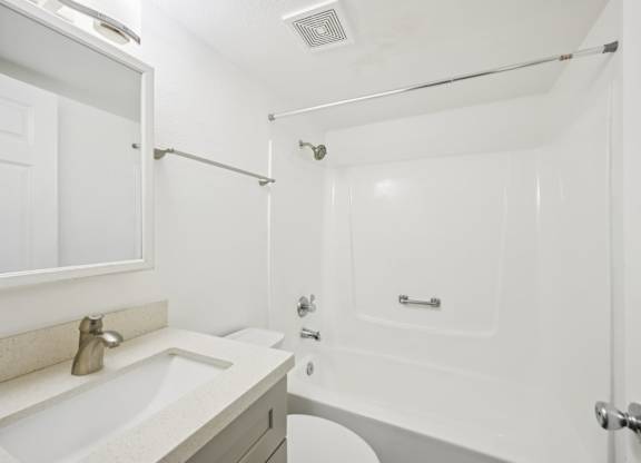 A white bathroom with a sink, mirror, and shower.