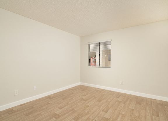A room with wooden flooring and a window with blinds.