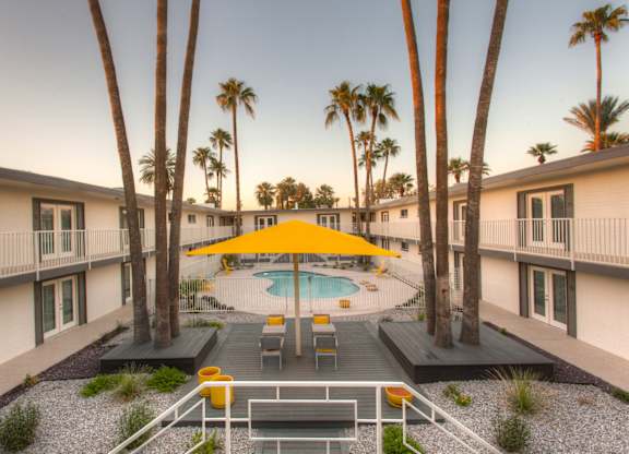 A community pool surrounded by palm trees and a yellow umbrella.