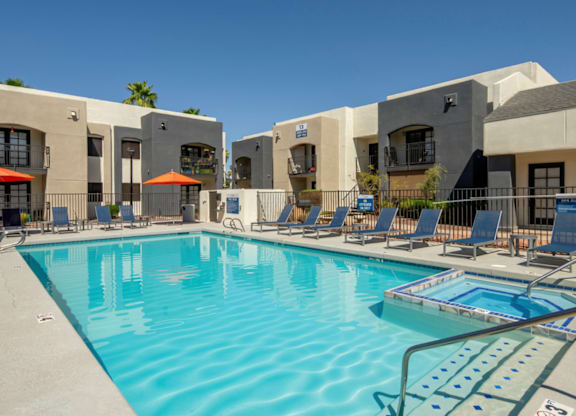A swimming pool surrounded by lounge chairs and umbrellas in front of a building.